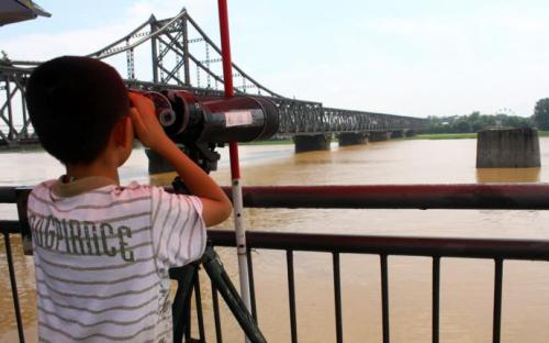 游客站在鸭绿江断桥上，用望远镜窥视对岸的朝鲜。